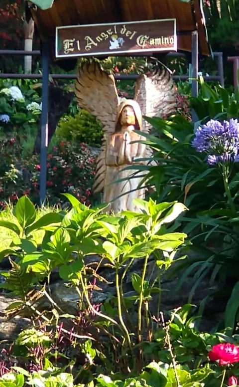 El Ángel del Camino, escultura tallada en madera entre las flores del jardín