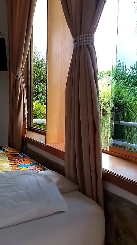 Ventana con cortinas y vista al jardín desde la cama