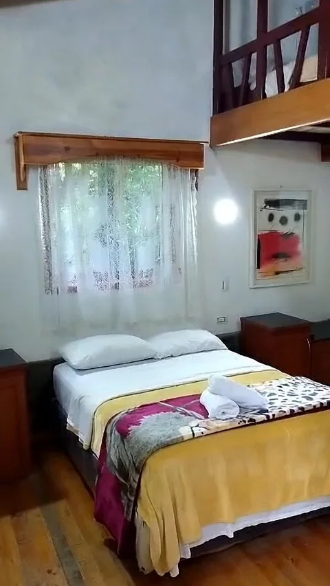 Cama matrimonial bajo una ventana con cortinas blancas
